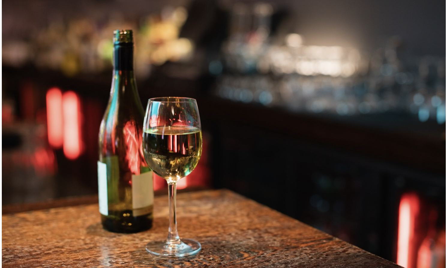 A glass of white wine next to a bottle of wine