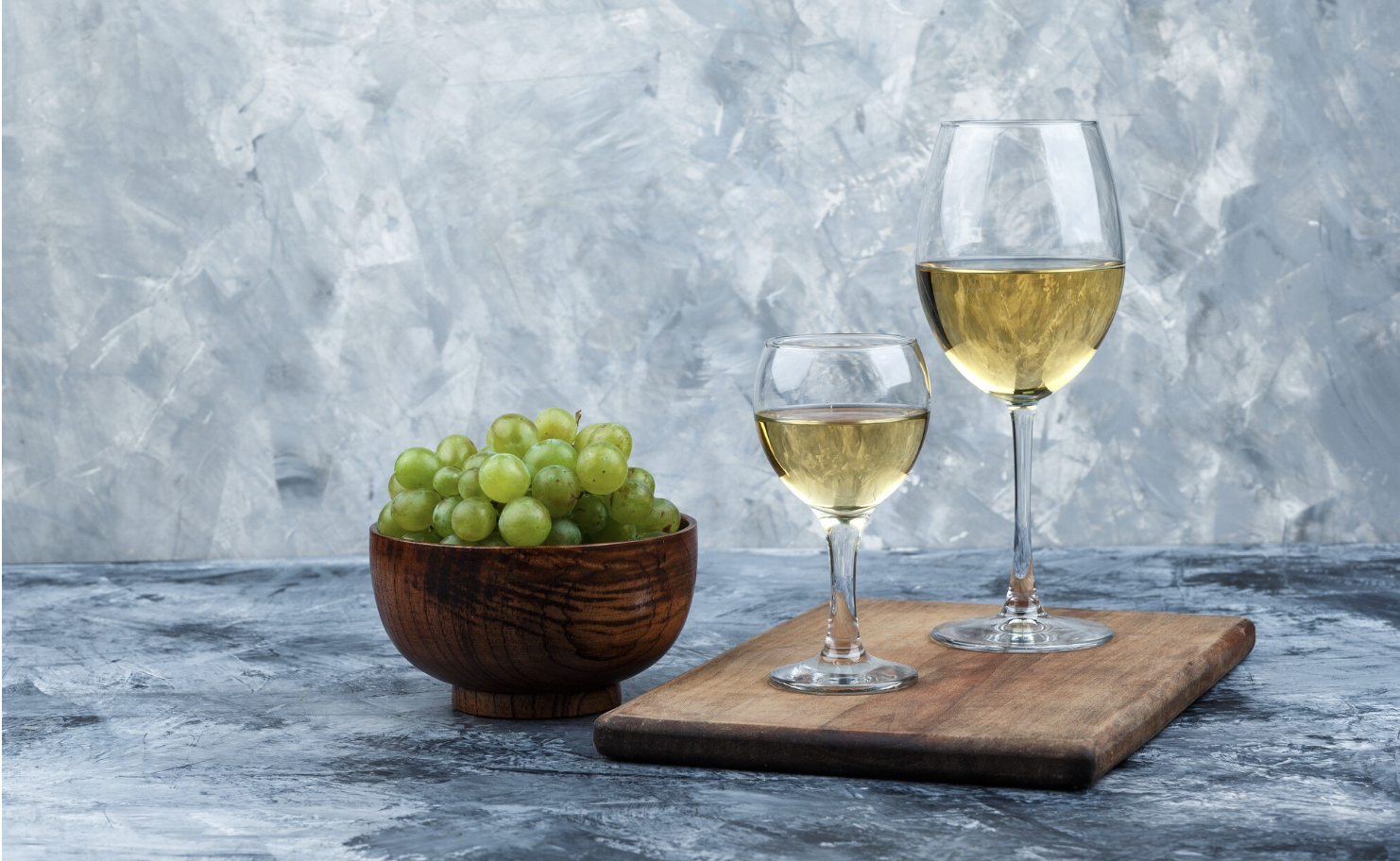 two glasses of white wine next to a bowl of grapes