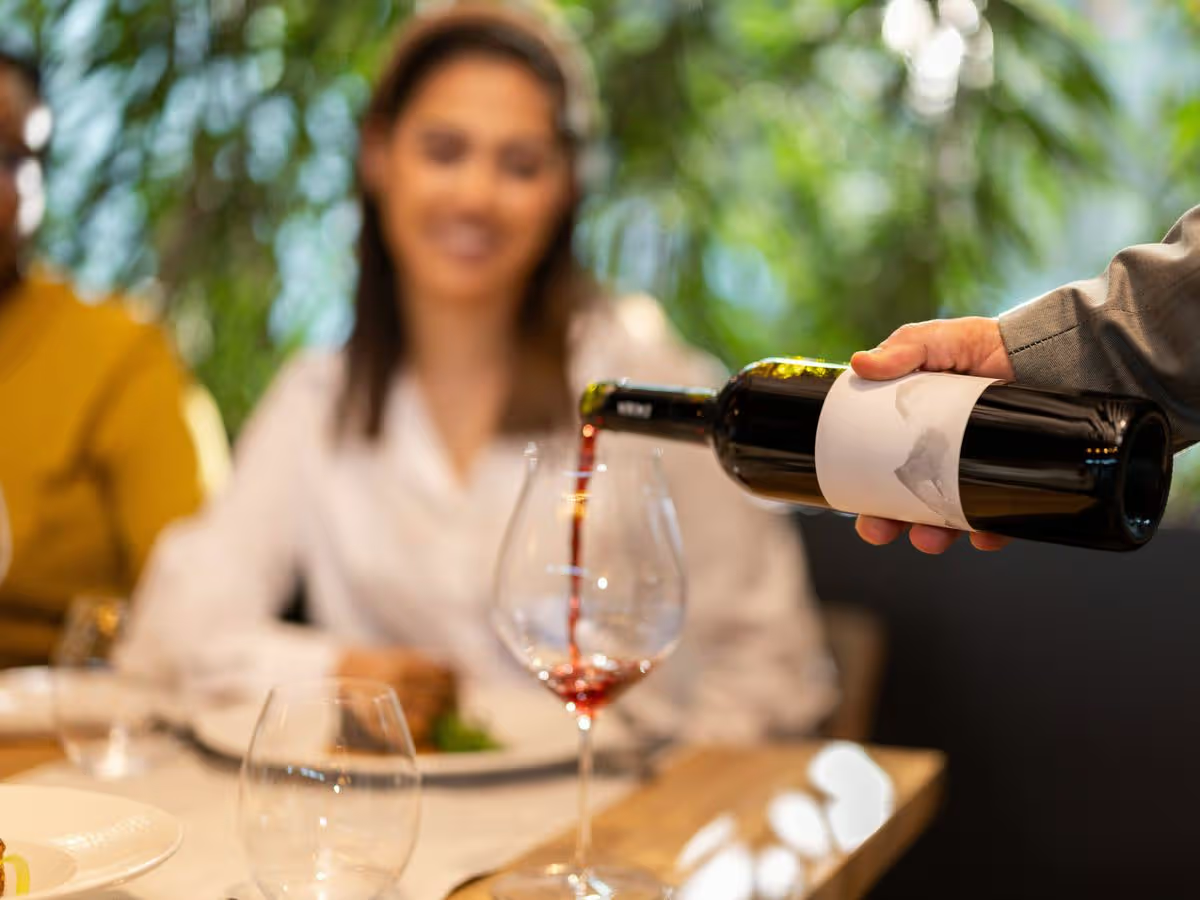 A glass of red wine being poured for a woman at a wine bar