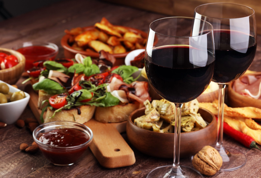 Two glasses of red wine next to a variety of cooked foods.