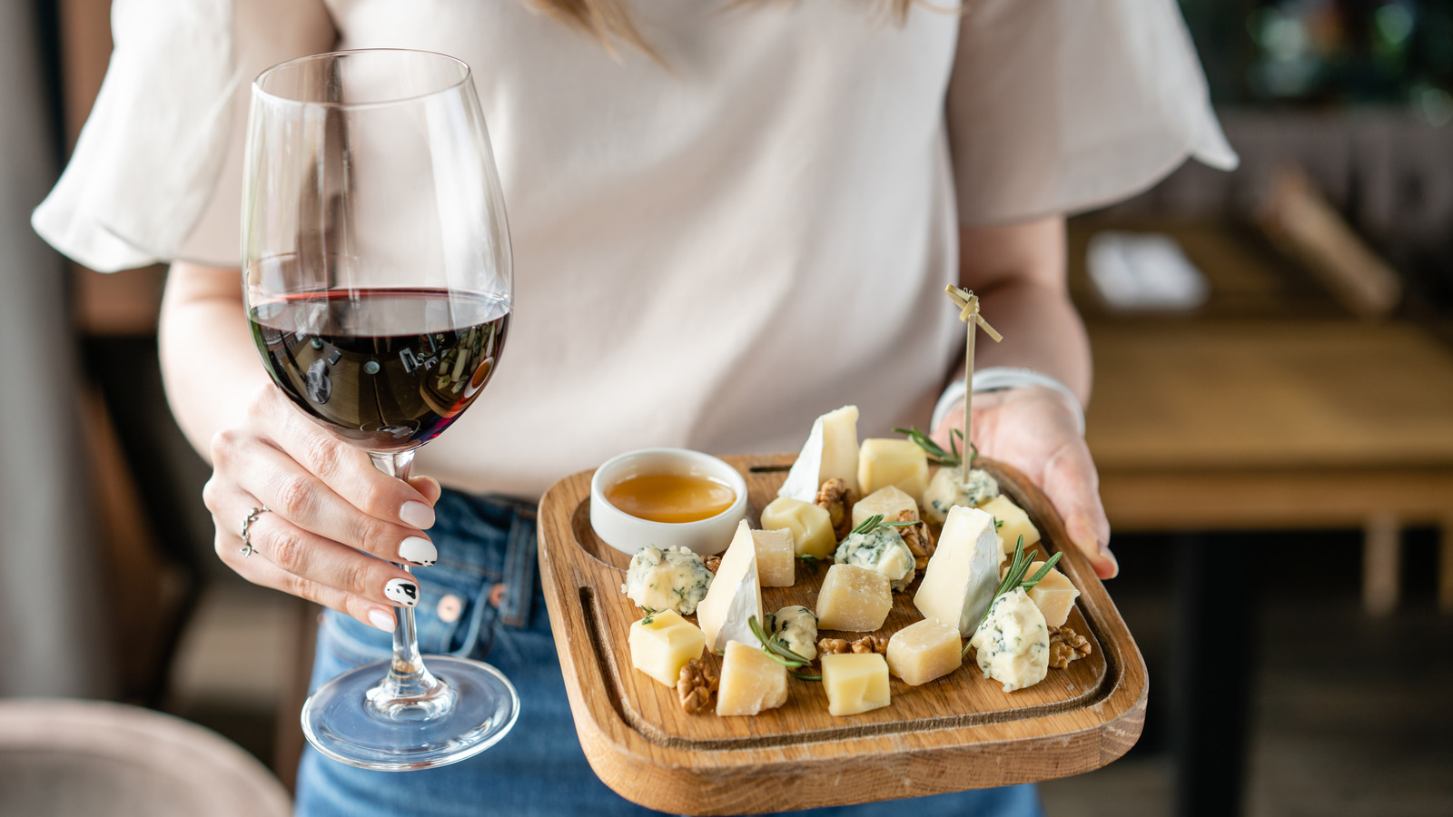 A woman holding a glass of red wine and a cheese board