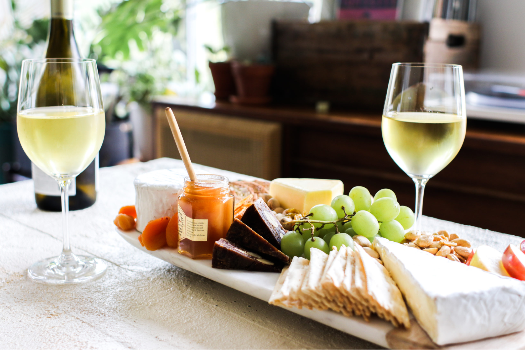 Two glasses of white wine with a grazing board with cheese and fruits