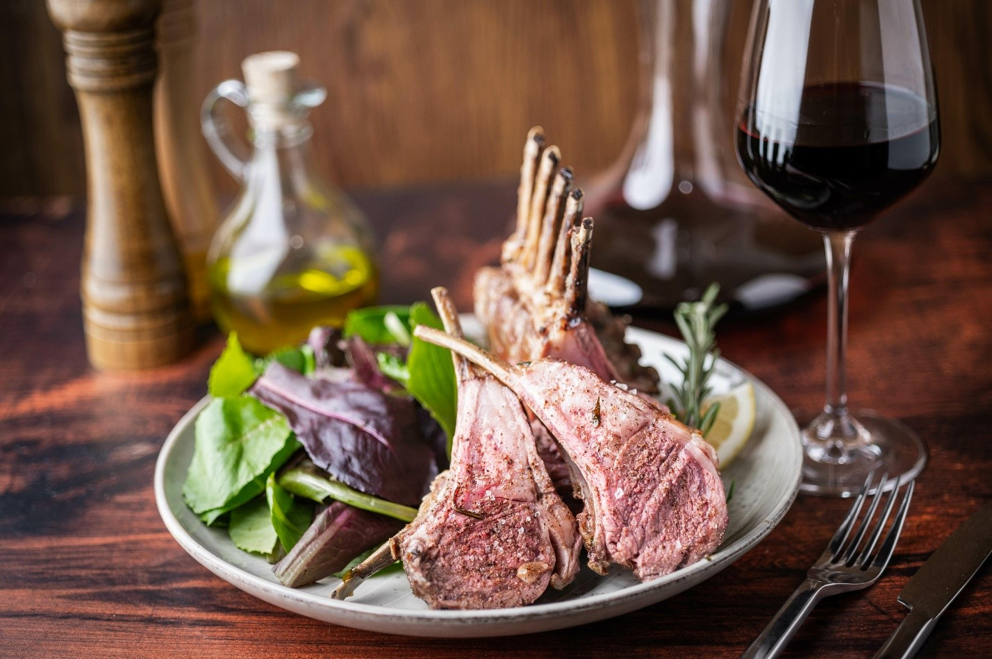 A plate of lamb cutlets and salad next to a glass of red wine